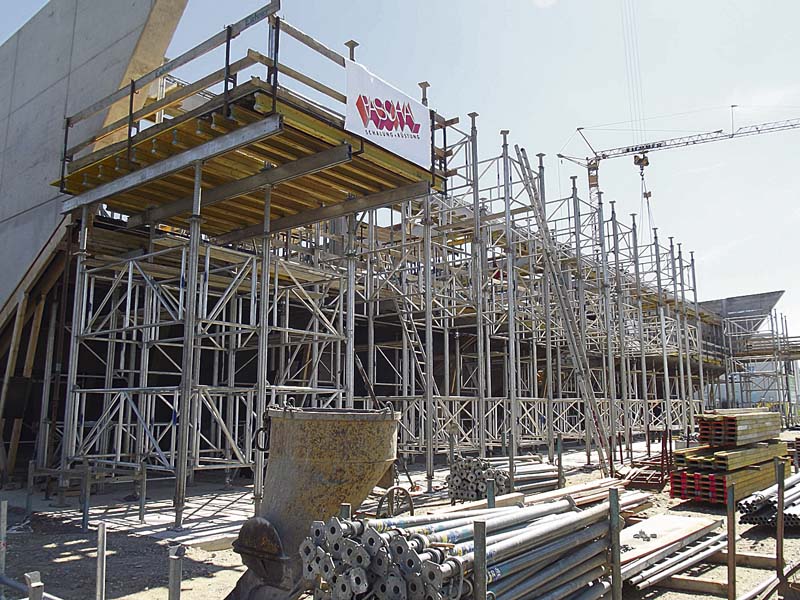 Um das auskragende Stahlbetonflachdach und die geneigten Attika mit rund 49,00 Metern schalen zu können wurden zur Lastabtragung Gerüsttürme aus dem Alu-Traggerüstsystem Gass mit 4.200 m³ Unterstützungsvolumen montiert.